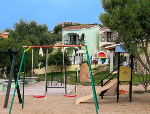 Ein Spielplatz mit Schaukeln und einer Rutsche, umgeben von Bäumen und Gebäuden.