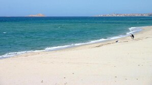 A beach with clear water, a distant island, and a person walking along the shore. - Stunning Sea View Apartment for 4 (Badesi)