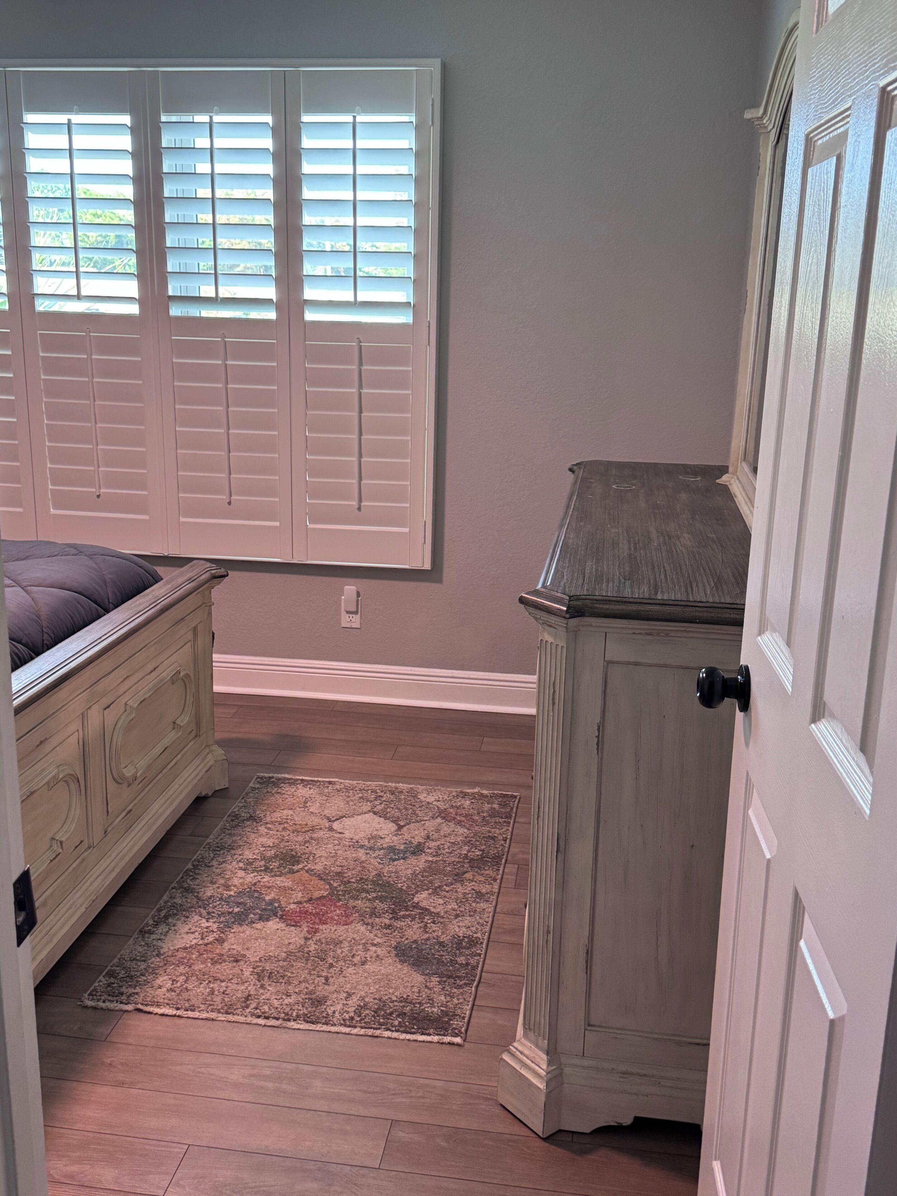A bedroom with a bed, a dresser, a window with blinds, and a rug.