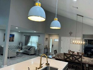 A modern living room with a marble island, grey sofas, and pendant lighting.