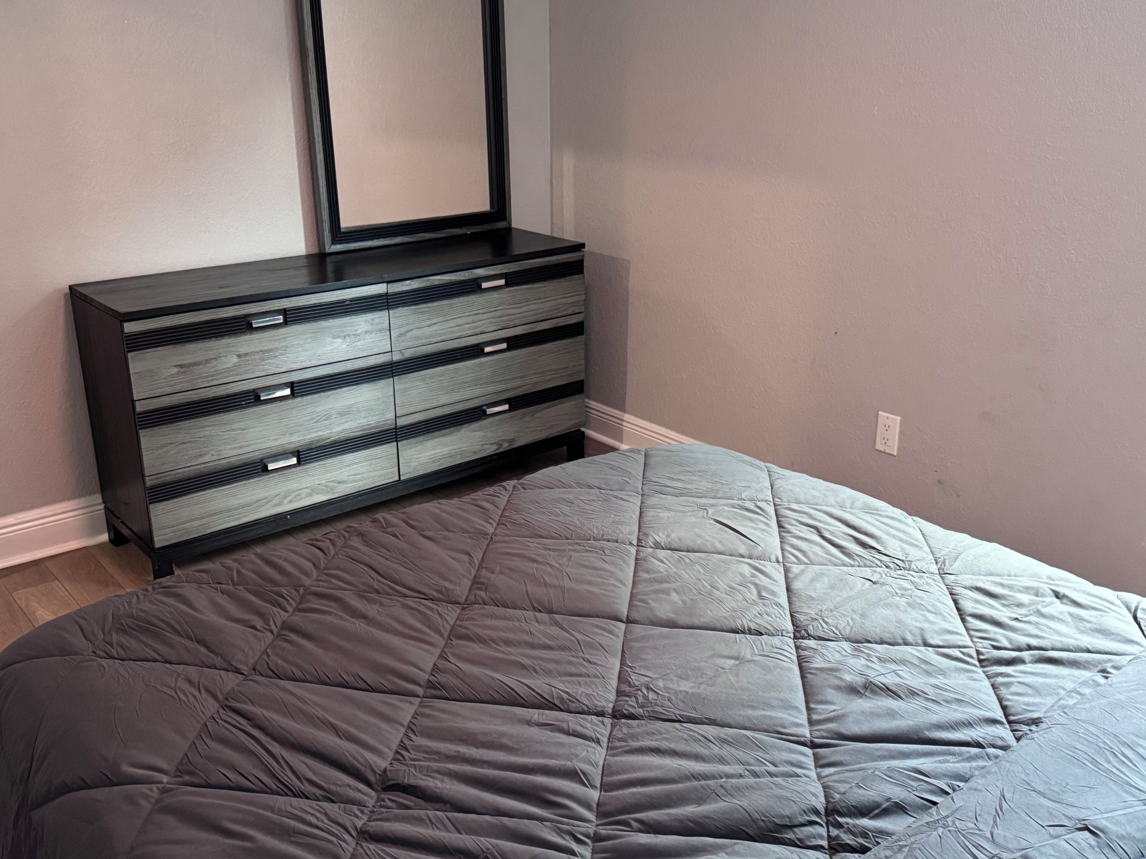 Un dormitorio con cama, cómoda y espejo montado en la pared.