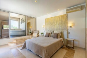 Una camera da letto moderna con un letto grande, un bagno con vasca e una porta vetrata scorrevole che dà su un balcone.