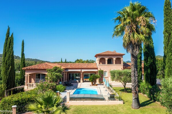 Una villa in stile mediterraneo con piscina, portico coperto e vista sul paesaggio circostante.