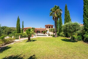 Una villa con tetto in tegole, circondata da un prato curato e alti cipressi.