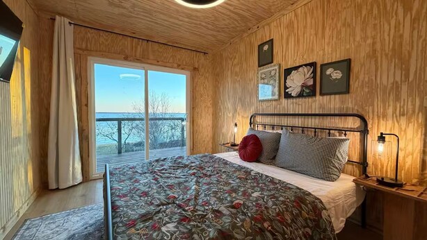 Una camera da letto con un letto, una ventola a soffitto, un comodino con una lampada e una finestra vista all'esterno.
