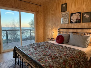 Une chambre à coucher avec un lit, une table de chevet, une lampe et une vue sur l’extérieur.