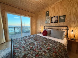 Une chambre avec un grand lit, des murs en bois, une vue à travers une porte coulissante et des œuvres d’art encadrées accrochées au mur.