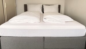 Een bed met een grijs hoofdeinde en witte beddengoed.