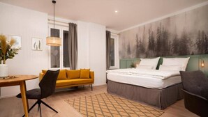 Quarto de hotel moderno com cama, sofá, escrivaninha e uma janela grande.