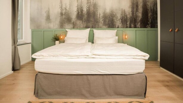 Quarto com cama, cabeceira verde, painel decorativo na parede e armário.