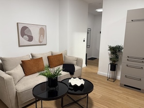 Un saló modern amb un sofà, dues taules de centre, una planta en test i un frigorífic.