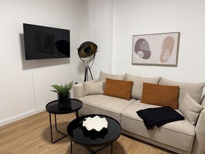 Ein Wohnzimmer mit einer Couch, zwei Beistelltischen, einer Stehlampe und Kunstwerken an der Wand.