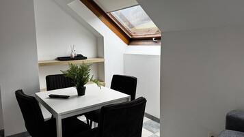 A dining area with a table, chairs, a potted plant, and a skylight.