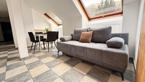 Un espace de vie moderne avec un canapé gris, une table à manger et des chaises, ainsi qu’une lucarne.
