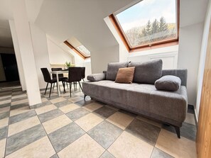 Un espacio habitable moderno con un sofá gris, una mesa de comedor con sillas y un tragaluz.