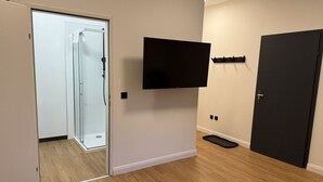 A room with a wooden floor, a glass door leading to a shower, a mounted flat-screen TV, and a dark door. - Faraway Homes Studio Semmering #302 (Spital am Semmering)