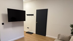 A room with a flat-screen TV mounted on the wall, a black door, a beige sofa, and a small plant. - Faraway Homes Studio Semmering #302 (Spital am Semmering)