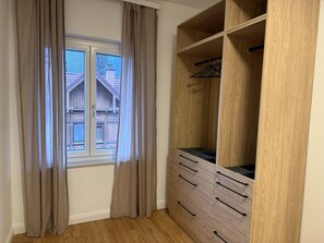 Una habitación con ventana, armario de madera y vista a un edificio.
