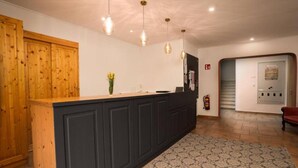 A reception area with a wooden counter, dark cabinets, hanging pendant lights, a patterned rug, and a fire extinguisher. - Faraway Homes Studio Semmering #301 (Spital am Semmering)