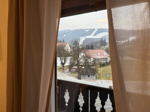 A window with curtains, a view of a town with houses and a mountain in the background. - Faraway Homes Studio Semmering #304 (Spital am Semmering)