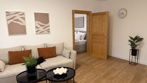 A living room with a sofa, two side tables, a potted plant, a wooden door, and a clock on the wall. - Faraway Homes Studio Semmering #304 (Spital am Semmering)