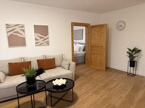 A living room with a sofa, two coffee tables, a potted plant, and a wooden door leading to another room. - Faraway Homes Studio Semmering #304 (Spital am Semmering)