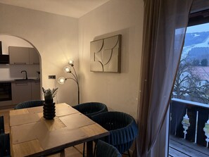 A dining area with a wooden table, chairs, a vase with plants, a wall-mounted abstract art piece, and a view of a snowy landscape through a window. - Faraway Homes Studio Semmering #304 (Spital am Semmering)