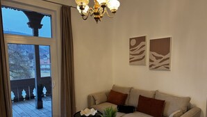 Een woonkamer met een bank, twee bijzettafels, een kroonluchter en uitzicht door een glazen deur.