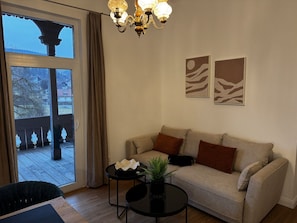 Una sala de estar con un sofá, dos mesitas auxiliares, una araña y vistas a través de un ventanal.