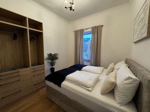 Ein Schlafzimmer mit einem Bett, einem Holzschrank, einer Topfpflanze und einem Fenster mit Vorhängen.