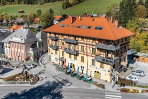 En traditionell byggnad med korsvirkesfasad och ett rött tegeltak, flera balkonger och en utsikt över gatan med parkerade bilar och ett övergångsställe.