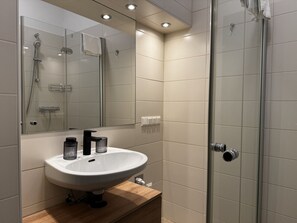 Un baño moderno con ducha de vidrio, un lavamanos blanco con un espejo encima y una encimera de madera.