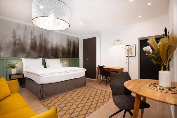 Ein Schlafzimmer mit Bett, Schreibtisch, Stuhl, Esstisch und einer Wand mit Waldbild.