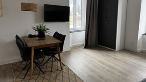 A room with a wooden dining table, black chairs, a flat-screen TV mounted on the wall, a large wardrobe, and a window with curtains. - Faraway Homes Studio Semmering #105 (Spital am Semmering)