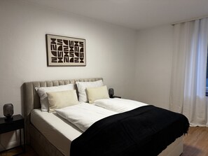 Ein Schlafzimmer mit Bett, Nachttisch, Lampe und einem Wandbild.
