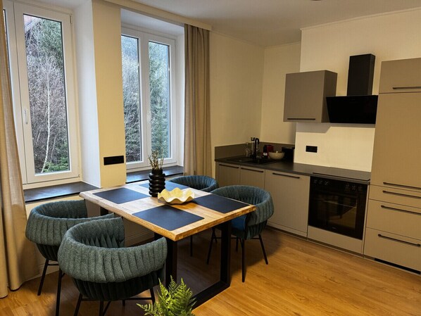 A modern kitchen with a dining area, large windows, and a view of trees.