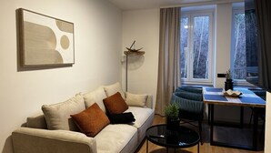 Een woonkamer met een bank, een eettafel, een vloerlamp en een raam met gordijnen.