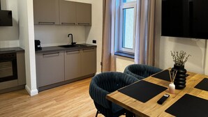 Eine moderne Küche mit grauen Schränken, einem schwarzen Spülbecken und einem Fenster mit Vorhängen. Es gibt einen Essbereich mit einem Holztisch, zwei Stühlen und einer Vase mit Ästen.