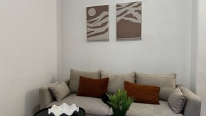 Ein Wohnzimmer mit einer Couch, zwei Kissen, einem kleinen runden Tisch, einer Topfpflanze und zwei Wandbildern.