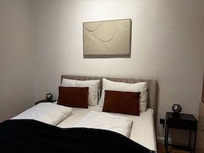 Ein ordentlich bezogenes Bett mit weißer und brauner Bettwäsche, ein Kopfteil und ein Nachttisch mit Lampe.