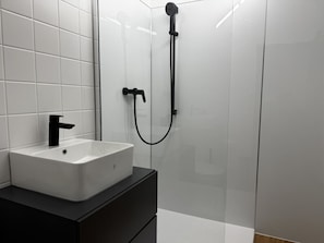 Ein modernes Badezimmer mit einem weißen Waschbecken, einem schwarzen Wasserhahn und einer Dusche mit einem schwarzen Duschschlauch.