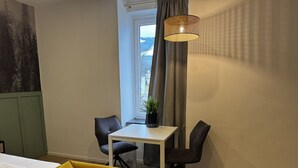 Een kamer met een bed, een eettafel met stoelen, een hanglamp en een raam met gordijnen.