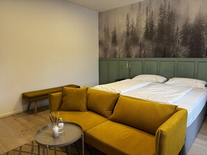 A room with a bed, a sofa, a small table, and a wall with a forest mural.