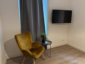 Ett rum med en gul fåtölj, ett litet bord med en växt och en TV som är monterad på väggen.