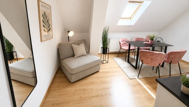 En moderne opholdsstue med sofa, spisebord med stole, et spejl og et ovenlysvindue.