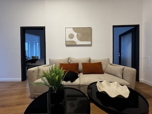 Uma sala de estar moderna com um sofá, duas mesas laterais, uma planta e uma obra de arte abstrata pendurada na parede.