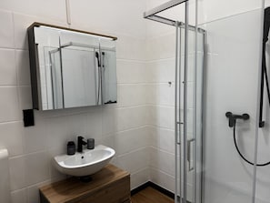 Casa de banho com lavatório branco, espelho e cabine de duche em vidro.
