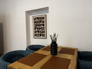Ein Zimmer mit Holztisch, blau gepolsterten Sitzmöglichkeiten und einer schwarzen Vase mit Ästen.