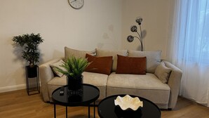 Un soggiorno con un divano, due tavolini, una pianta in vaso, una sveglia a parete e un lampadario decorativo.