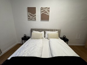 Ein Doppelbett mit weißer Bettwäsche, zwei Nachttische mit Lampen und zwei abstrakte Wandbilder.
